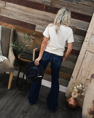 Back view of dark wash flare jeans styled with a neutral basic tee and black western hat for a chic boutique outfit with modern western-inspired fashion.