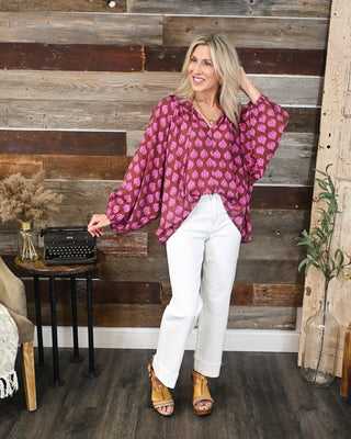 Brown and bright pink printed long sleeve blouse with a relaxed fit and balloon sleeves, styled with white cuffed jeans for a chic fall boutique outfit.