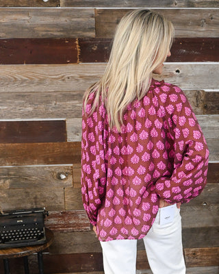 Brown and bright pink printed long sleeve blouse with relaxed fit and gathered neckline, styled with white jeans for a colorful fall boutique look.