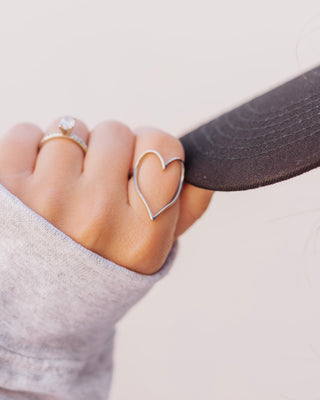 Close-up of a hand wearing a minimalist silver wire heart ring stacked next to a gold and diamond engagement ring.