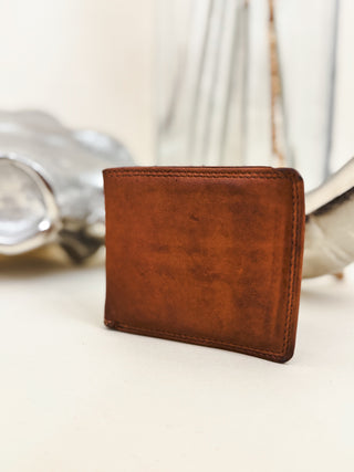 Rustic brown leather bifold wallet with a smooth finish, styled with western decor in the background.