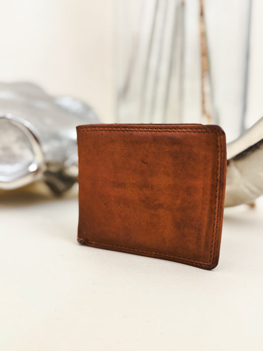 Rustic brown leather bifold wallet with a smooth finish, styled with western decor in the background.