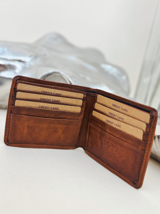 Open brown leather bifold wallet with multiple card slots and embossed Ranchero branding, styled with western decor in the background.