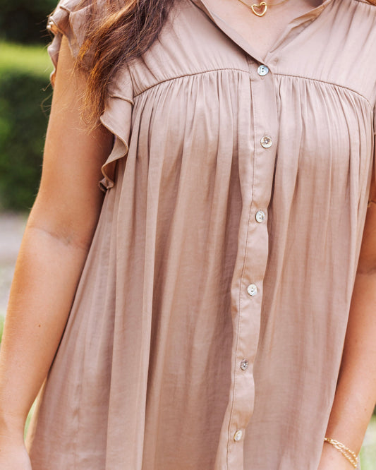 Close-up of a taupe button-front blouse with ruffle sleeves and pleated detailing, styled with delicate gold jewelry for a chic and feminine look.