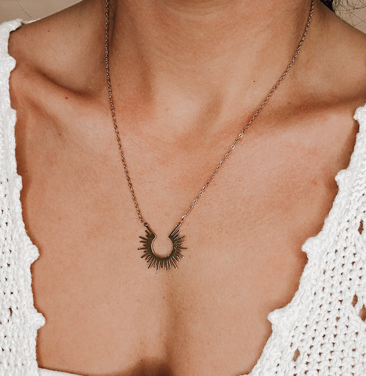 Close-up of woman wearing a bronze sunburst pendant necklace on a delicate chain. Boho-inspired jewelry piece with celestial design, perfect for layering or standalone styling.