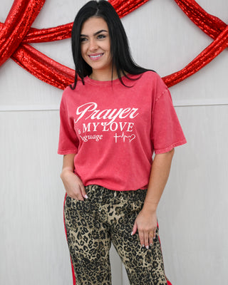 Woman wearing a red t-shirt with 'Prayer is my love language' text, standing against a decorative red and white background.