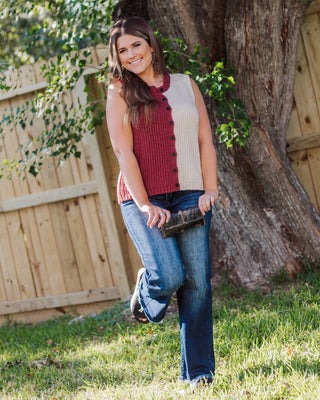 Woman wearing a sleeveless colorblock knit sweater vest in rust and cream with dark jeans and black shoes, styled outdoors for a cozy fall look.