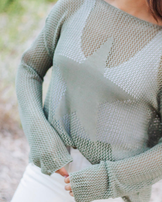 Olive green mesh knit sweater with oversized star detail, styled with white jeans for a trendy and casual look.