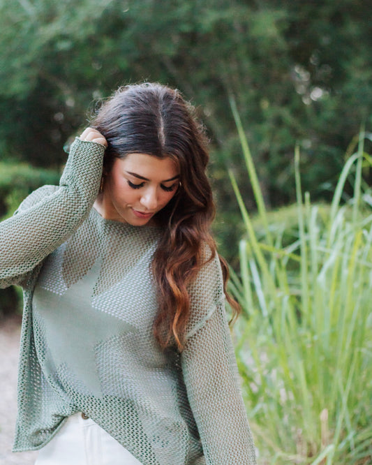 Woman wearing a sage green mesh knit sweater with star detail, paired with white jeans. Lightweight boho-chic style perfect for layering in spring or fall.