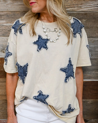 Beige oversized graphic tee with distressed denim star patches, relaxed fit casual boutique top styled with white pants—trendy patriotic outfit, comfy everyday women’s fashion