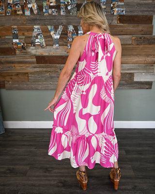 Women’s pink and white abstract print midi dress with halter tie neckline, tiered ruffle hem, and flowy silhouette shown from the back for a bold boutique look