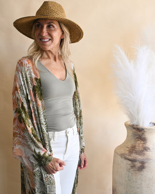 Women's tropical palm print kimono layered over a sage green tank top and white high-rise jeans. Lightweight boho cardigan with resort-inspired style and flowy sleeves.