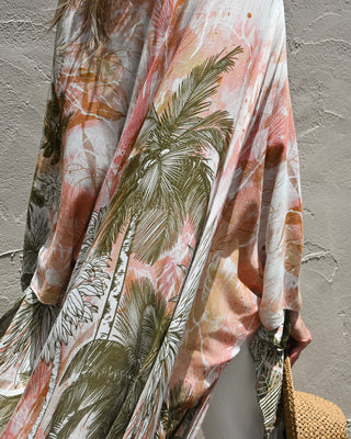 Women's tropical palm print kimono in soft blush pink, olive green, and ivory tones. Lightweight boho layering piece with flowy sleeves and resort-inspired style.