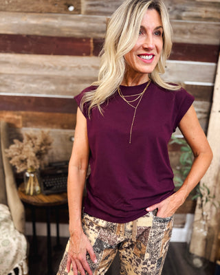 Women's burgundy cap sleeve crewneck top with a relaxed fit, styled with brown paisley patchwork pants and layered gold necklaces for a trendy casual fall outfit at MaKenzie Layne Boutique.