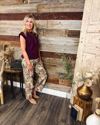 Women's burgundy cap sleeve top with a relaxed fit, styled with brown and cream paisley patchwork pants and tan flats for a casual fall outfit at MaKenzie Layne Boutique.