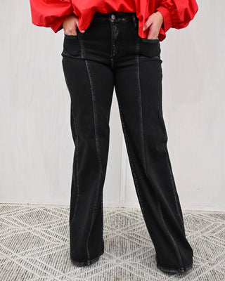 Person wearing black flared jeans and a red top on a light gray background