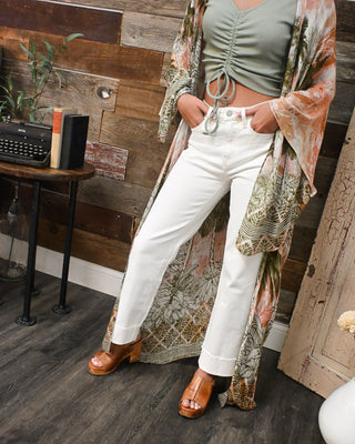 Person wearing a green top, white pants, and a patterned kimono in a room with wooden walls and a typewriter.