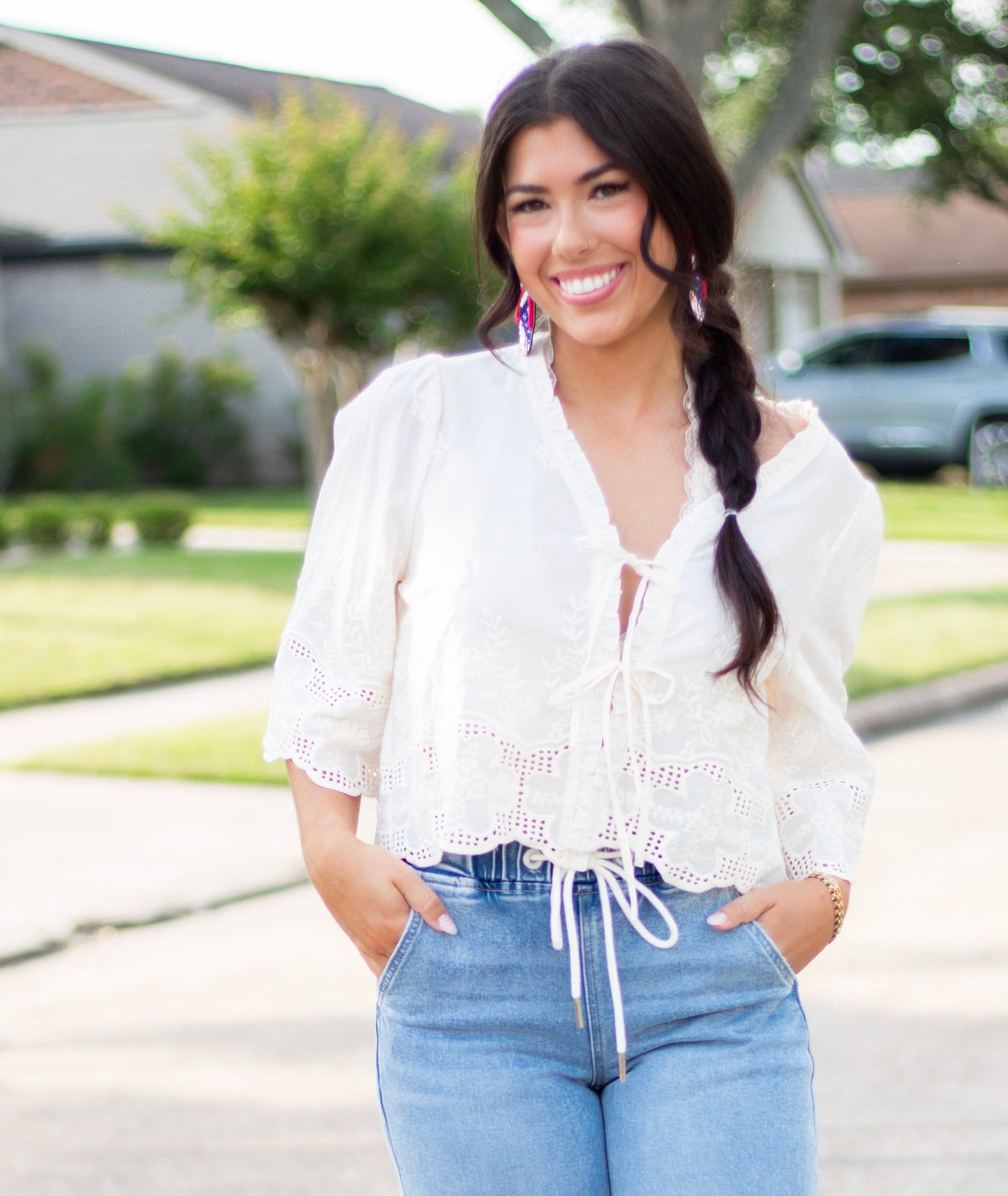 Woman wearing a white embroidered eyelet tie-front blouse with scalloped hem and puff sleeves, paired with high-rise light-wash denim. A feminine and breezy look perfect for spring and summer.