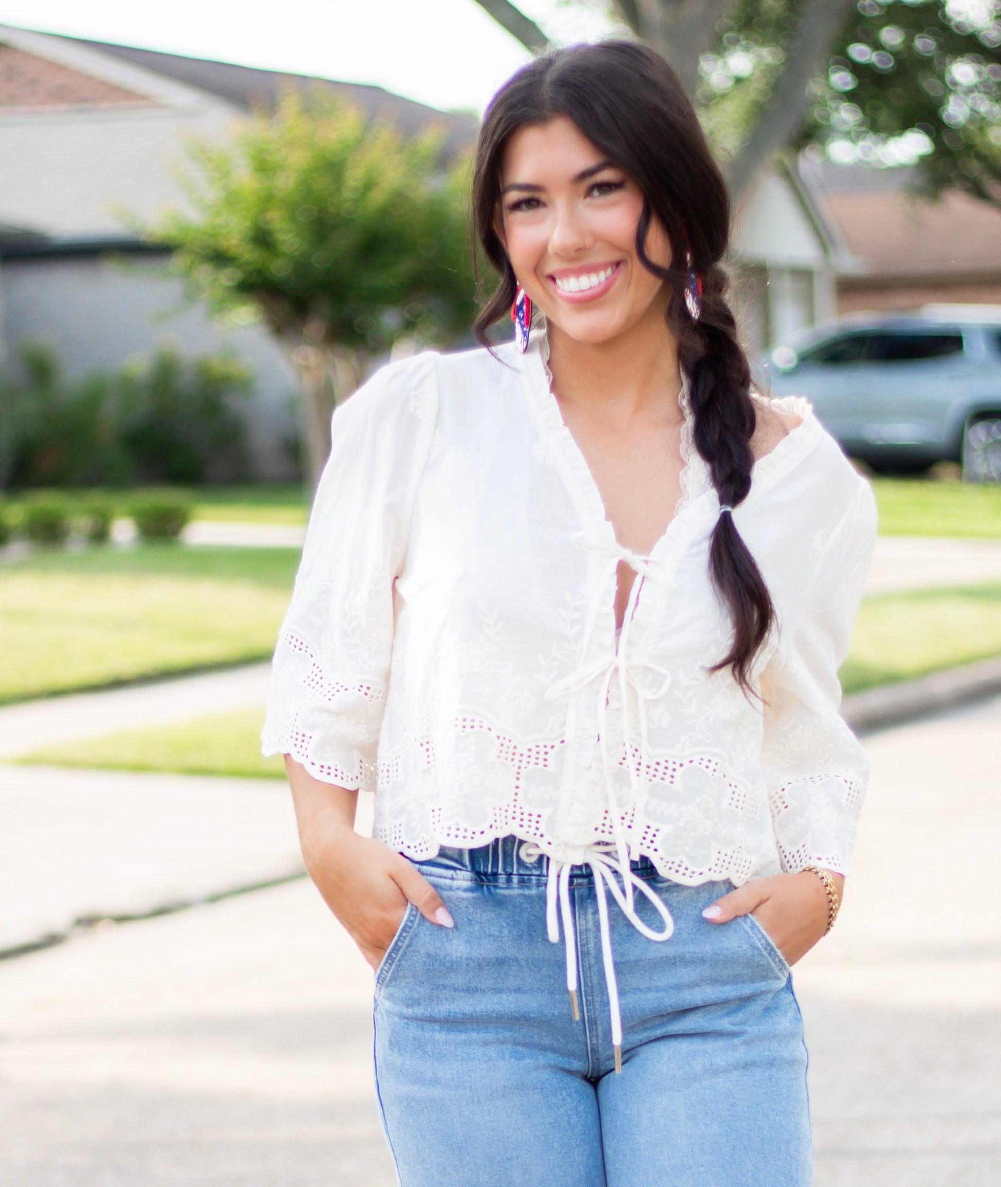 Woman wearing a white embroidered eyelet tie-front blouse with scalloped hem and puff sleeves, paired with high-rise light-wash denim. A feminine and breezy look perfect for spring and summer.