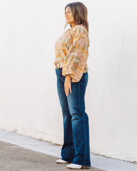 A woman models a chic, boho-print balloon sleeve top paired with high-waisted flare jeans with a frayed hem.