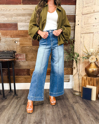 Women’s high-rise wide leg jeans in a medium wash with front seam detailing and relaxed fit, styled with an olive green jacket and white tank.