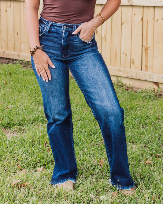 Front view of woman wearing high-waisted dark wash straight leg jeans with raw hem, styled with a fitted brown top and gold jewelry for casual chic style.