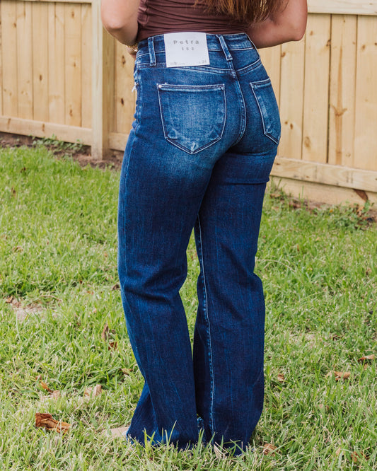 Back view of woman wearing high-waisted dark wash flare jeans with Petra 153 label, styled with a fitted brown top for a flattering casual look.