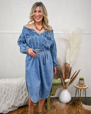 Model wearing an off-the-shoulder denim midi dress with button-down front, long balloon sleeves, chest pockets, and a matching denim belt for a cinched waist look.