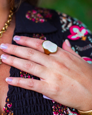 Close-up of a gold statement ring with an iridescent mother-of-pearl face, adding an elegant touch to a chic boho floral blouse and gold accessories.