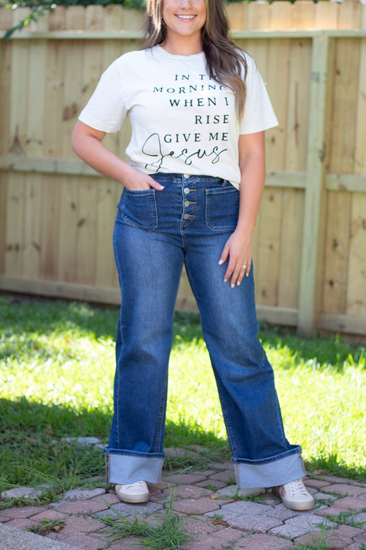 A woman models a graphic t-shirt with text, paired with high-waisted cuffed jeans and sneakers.