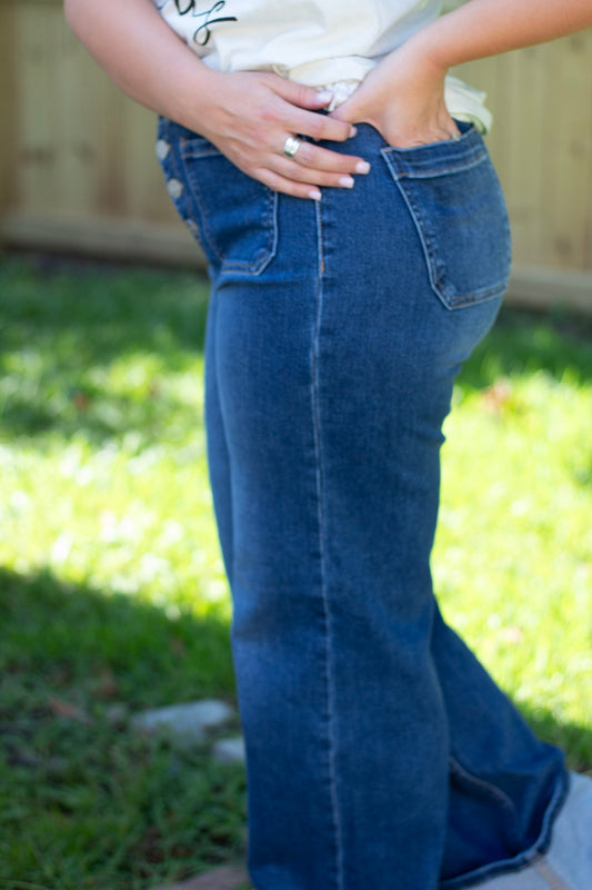 A close-up side view of high-waisted flare jeans with a button-fly closure and back pockets.