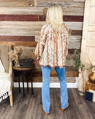 Back view of women’s boho floral print blouse with rust pom-pom trim and long sleeves, styled with light wash flare jeans for an effortless fall outfit.
