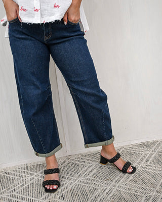 Person wearing blue jeans and black sandals on a patterned rug.