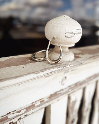 Close-up of polished silver teardrop hoop earrings with an open sculptural design and smooth curved finish, styled on a rustic vintage display at MaKenzie Layne Boutique.