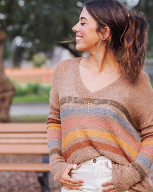 Woman wearing a cozy knit sweater with multicolor stripes in earth tones, paired with white jeans. Casual fall outfit with a soft, relaxed fit.