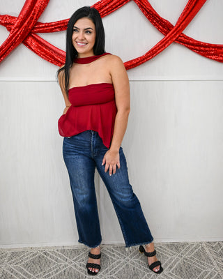 Woman wearing a red top and blue jeans standing against a white wall with red decorative elements.