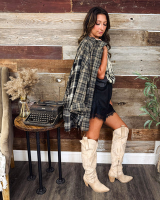 Women's charcoal and beige plaid flannel shacket styled over a vintage graphic tee, black lace-trim shorts, and cream knee-high western boots at MaKenzie Layne Boutique.