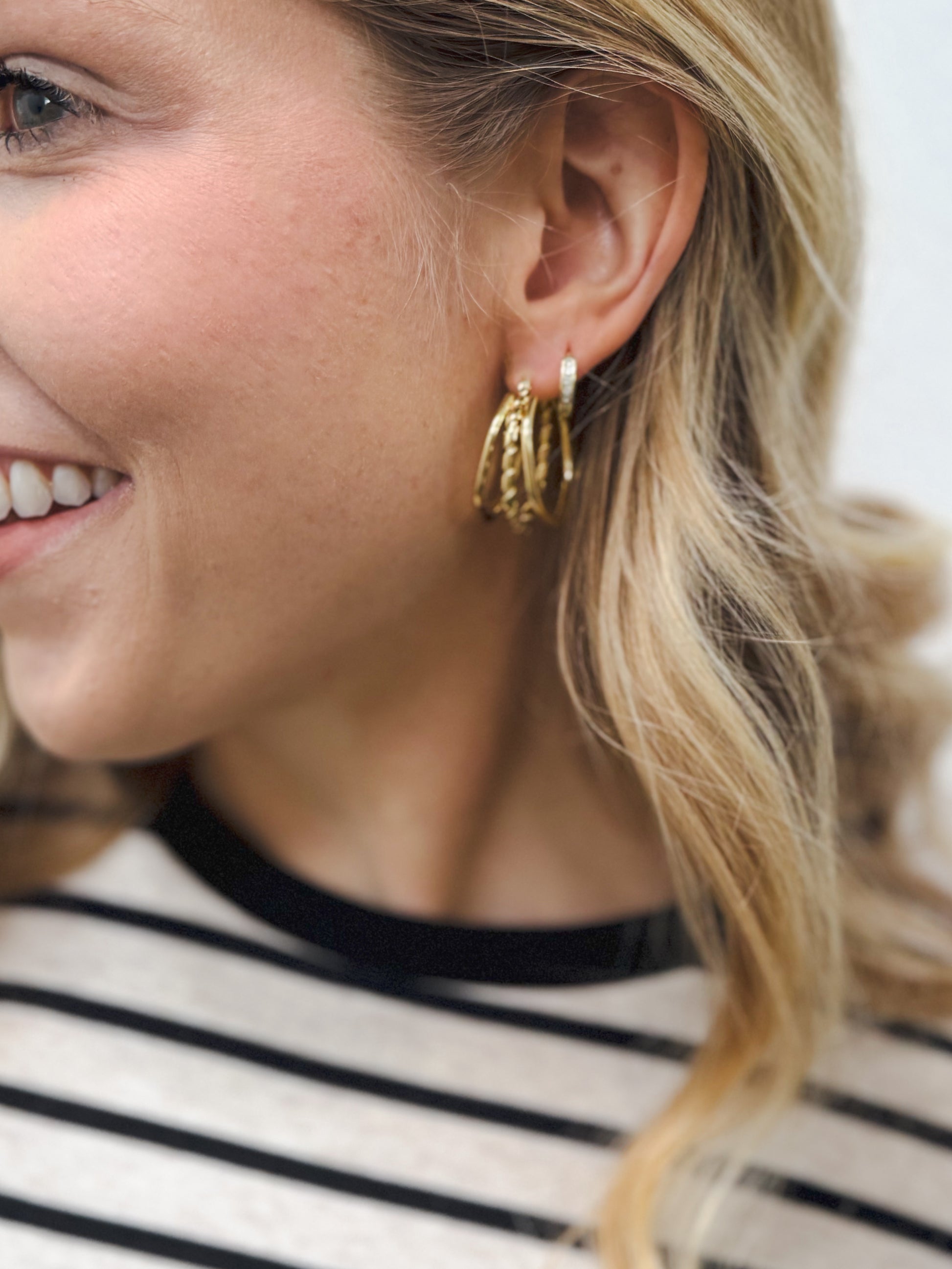 Close-up of a woman’s ear wearing multiple stackable gold hoop earrings in mixed textures and sizes, paired with a black-and-white striped top