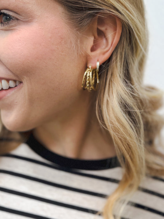 Close-up of a woman’s ear wearing multiple stackable gold hoop earrings in mixed textures and sizes, paired with a black-and-white striped top
