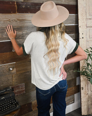 Women’s ivory micro stripe short sleeve top with dark green contrast cuffs, styled with dark wash jeans and a neutral wide brim hat for a casual fall look.