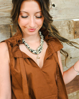 Cow print statement necklace with fabric-wrapped links and gold-tone charms, styled on a model with a brown ruffle-front blouse for a trendy Western-inspired look.